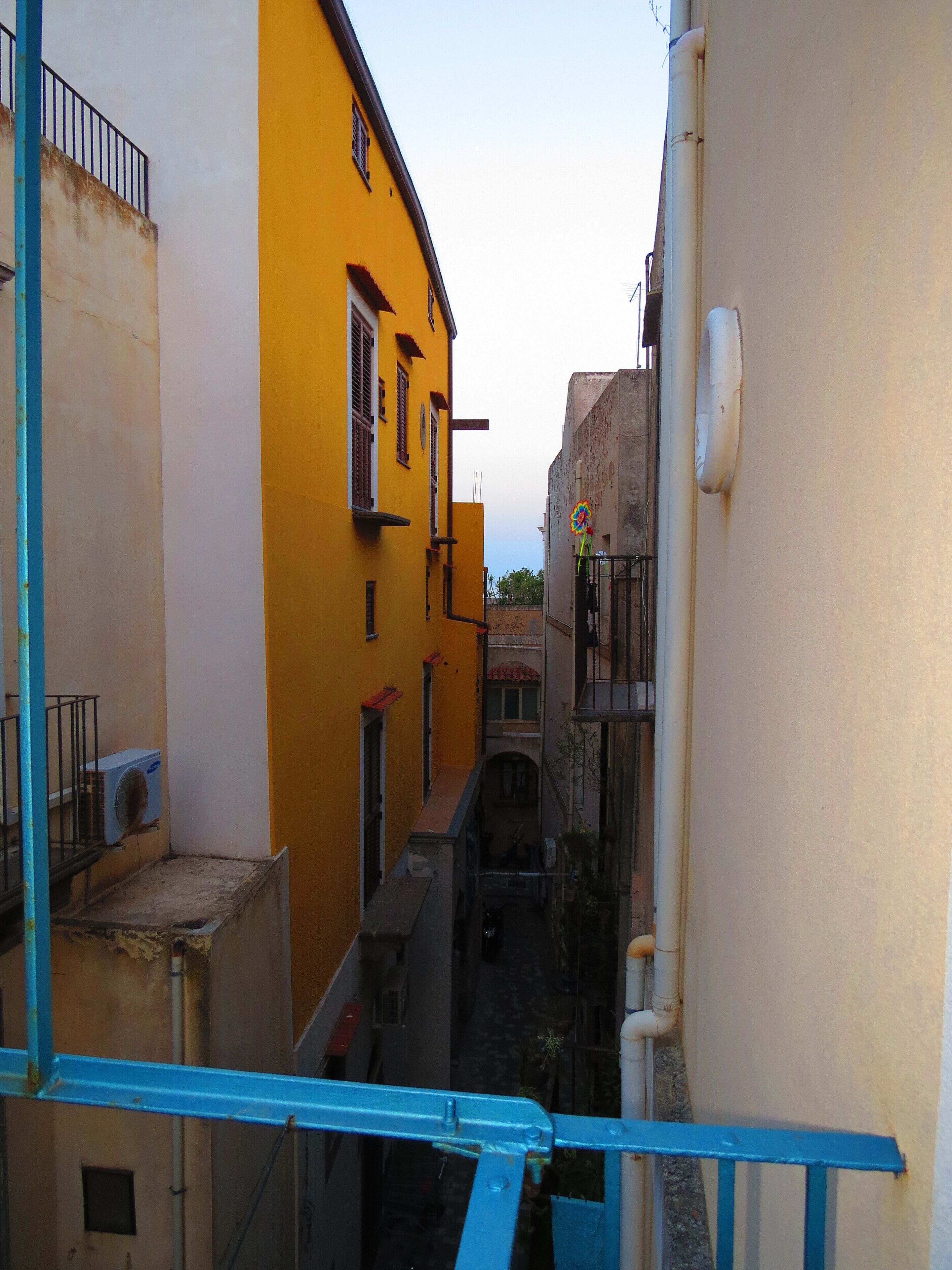 Um beco estreito entre edifícios, um com fachada amarela e outro branco à direita.