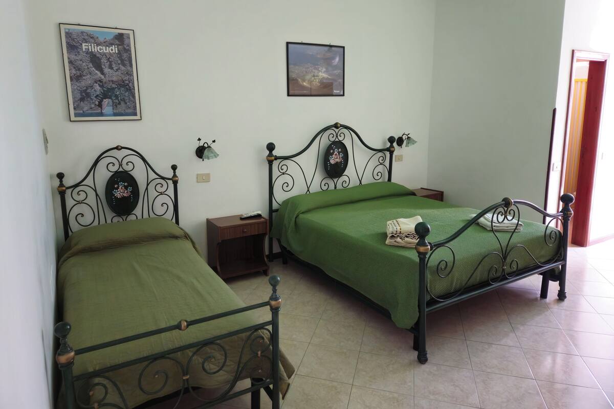 A bedroom with two metal-framed beds, a nightstand, a wall-mounted lamp, and a framed picture.