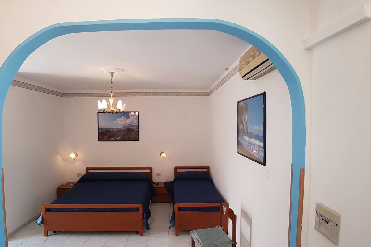 A bedroom with two wooden beds, a chandelier, wall-mounted lights, and two framed pictures.