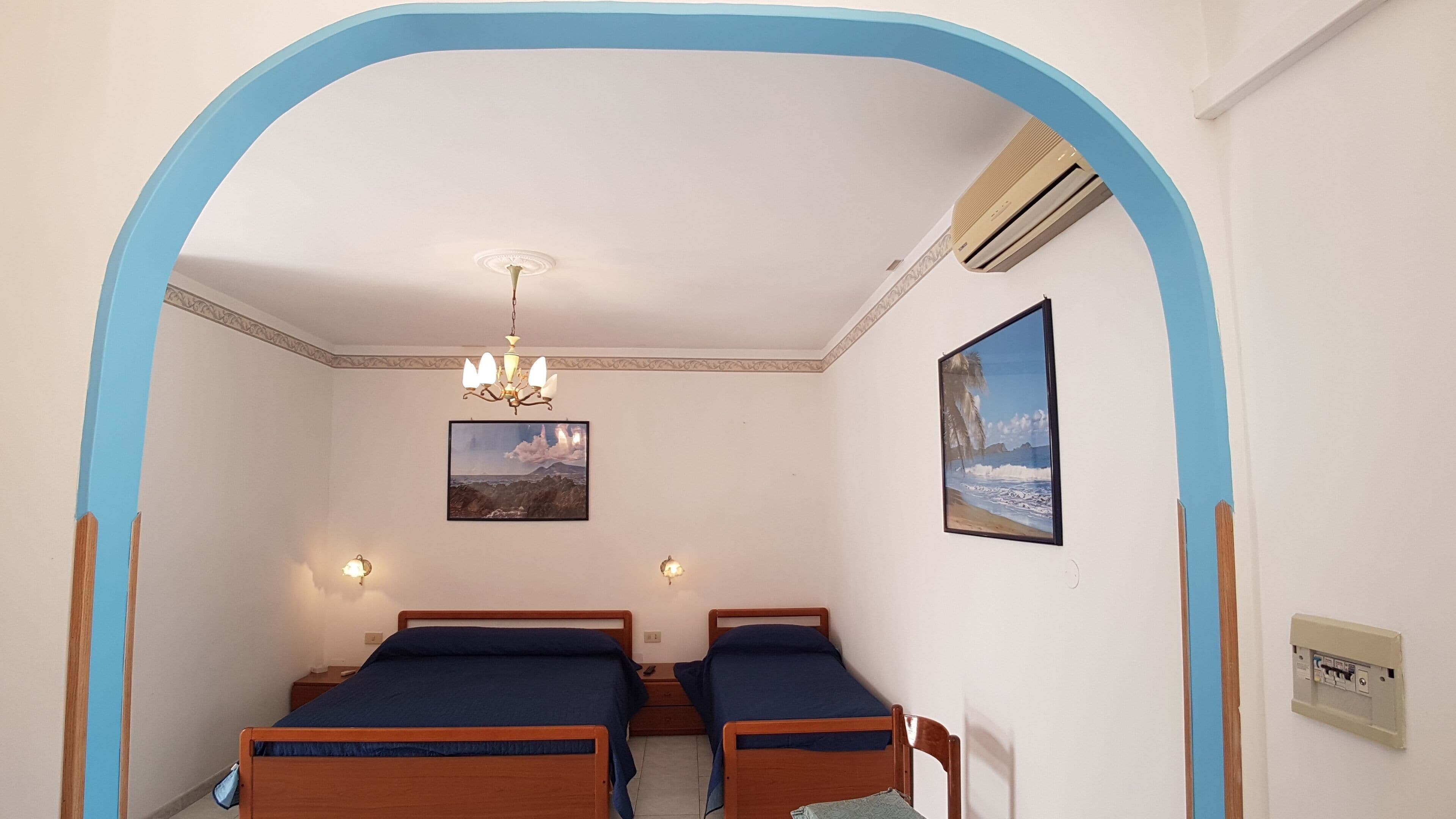 A room with two wooden beds, a chandelier, and a framed picture on the wall.