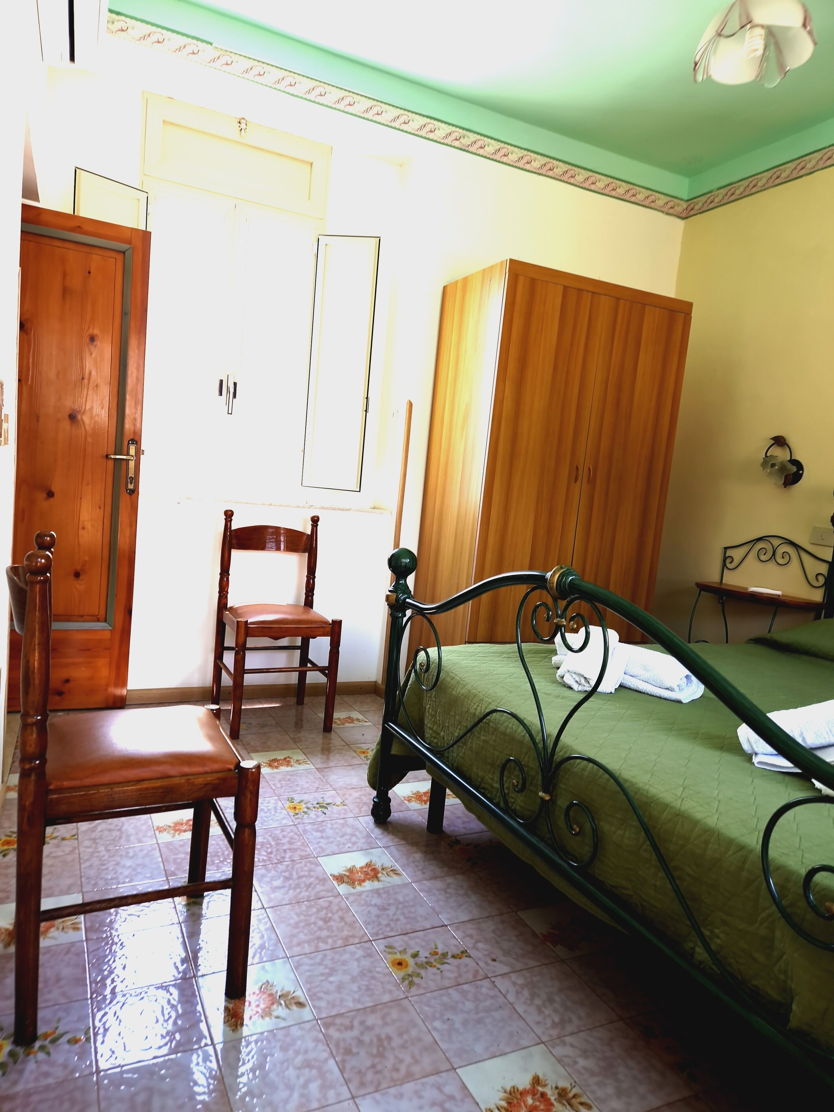 A bedroom with a bed, a wooden wardrobe, a wooden chair, and a desk.