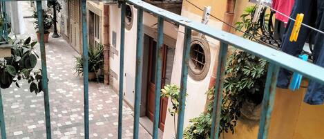 A narrow alleyway with potted plants and a balcony with clothes drying.