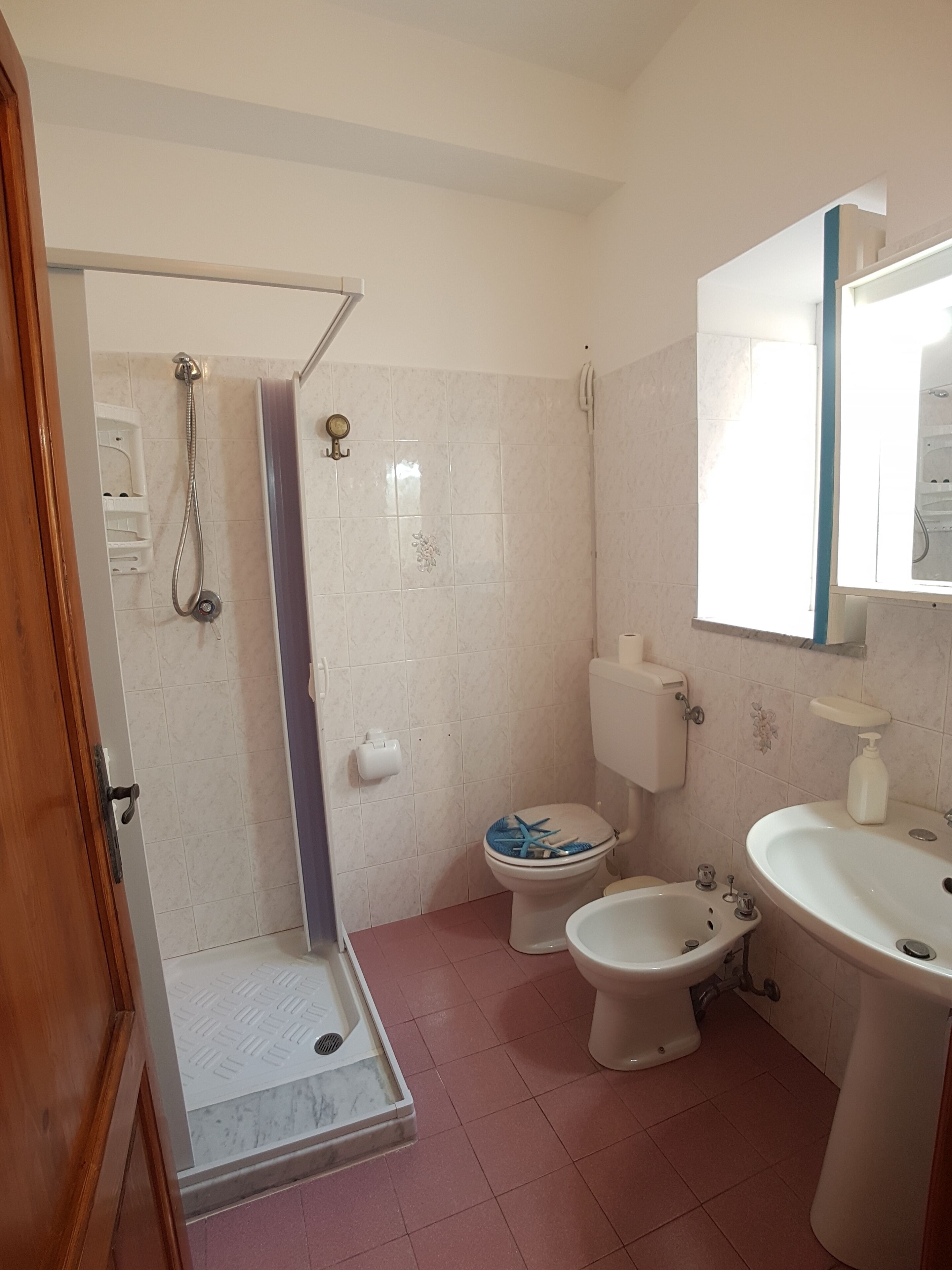 A bathroom with a shower, toilet, bidet, and sink.