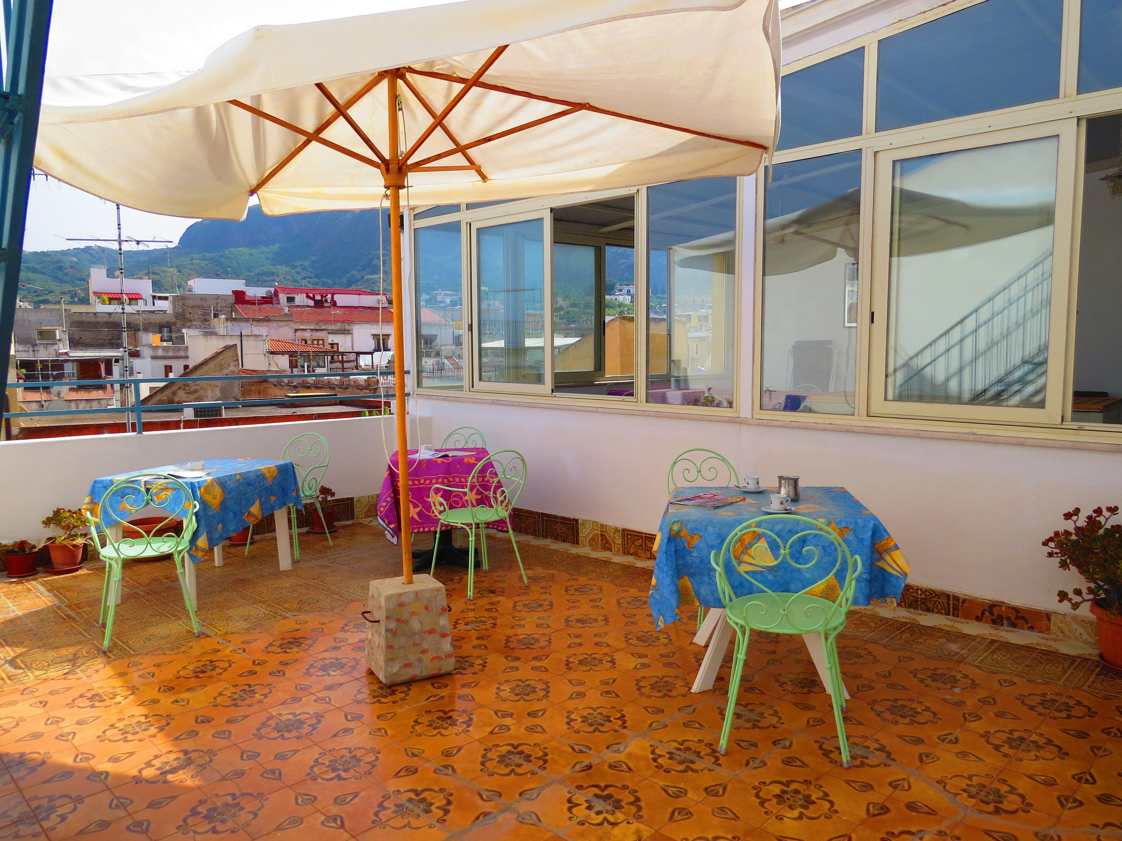 Un balcon avec une table et des chaises, un grand parasol et une vue sur les bâtiments en arrière-plan.