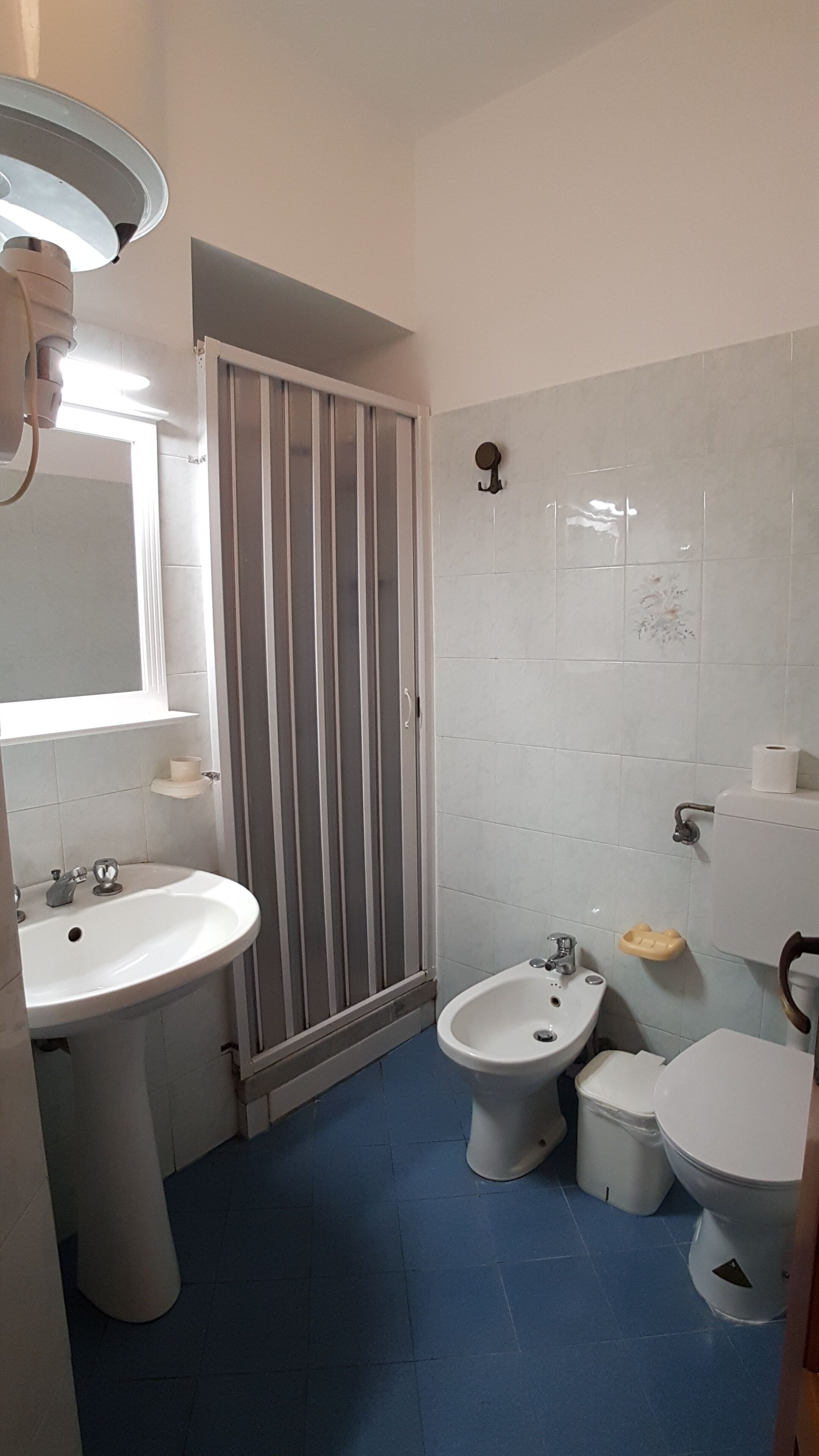 Une salle de bain équipée d’un lavabo, d’un bidet, de toilettes et d’une douche dont la porte est à rayures.
