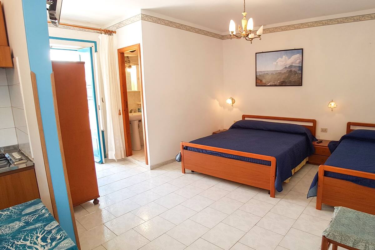 A bedroom with two wooden beds, a chandelier, a painting, and a bathroom visible through an open door.