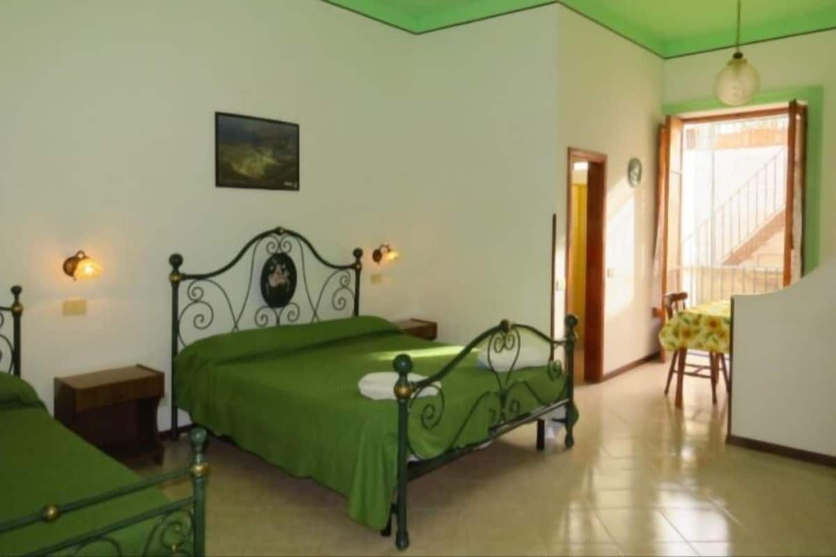 A bedroom with two beds, a nightstand, a wall-mounted lamp, a framed picture, and a staircase leading to another room.