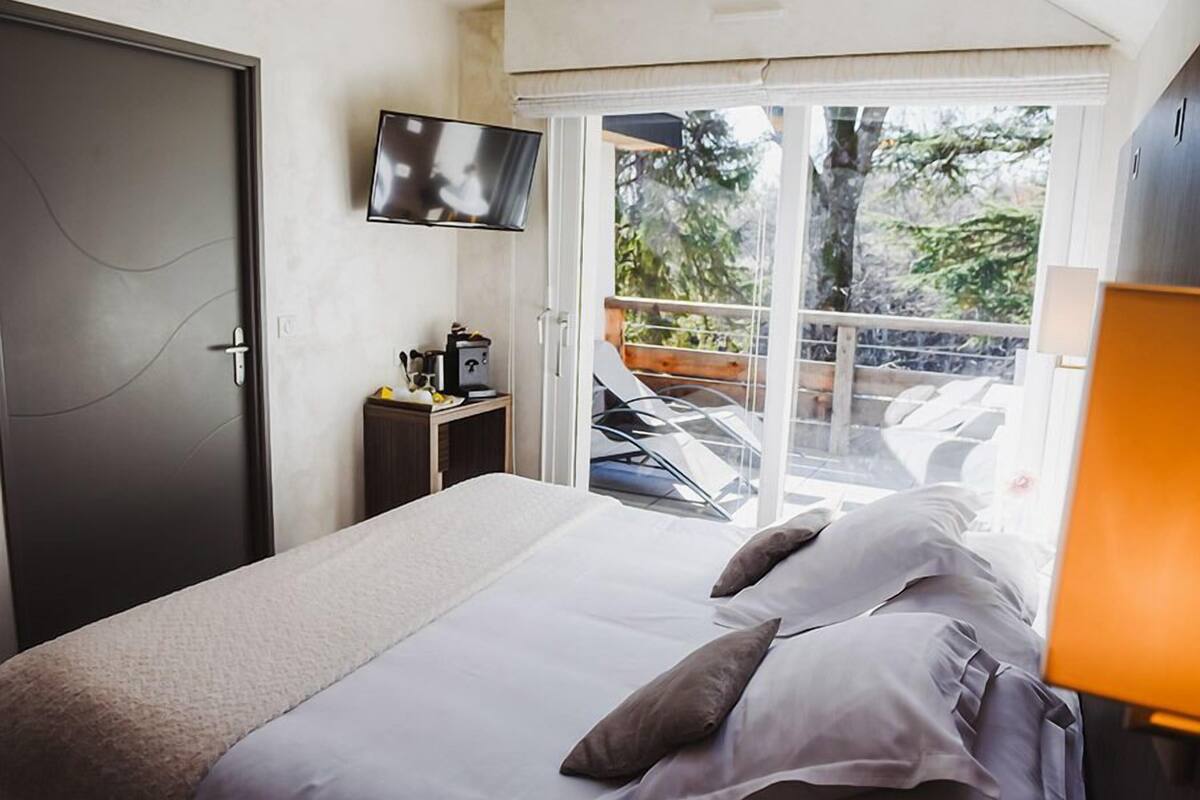 Een hotelkamer met een bed, een televisie, een klein tafeltje met een koffiezetapparaat en een balkon met buitenmeubilair.