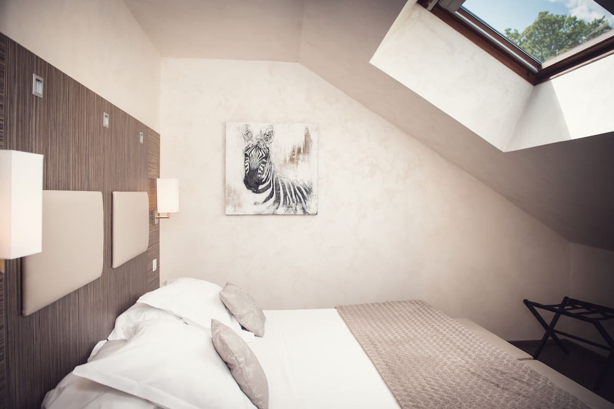 Een slaapkamer met schuine wand, een schilderij van een zebra aan de muur, een bed met witte lakens en een dakraam.