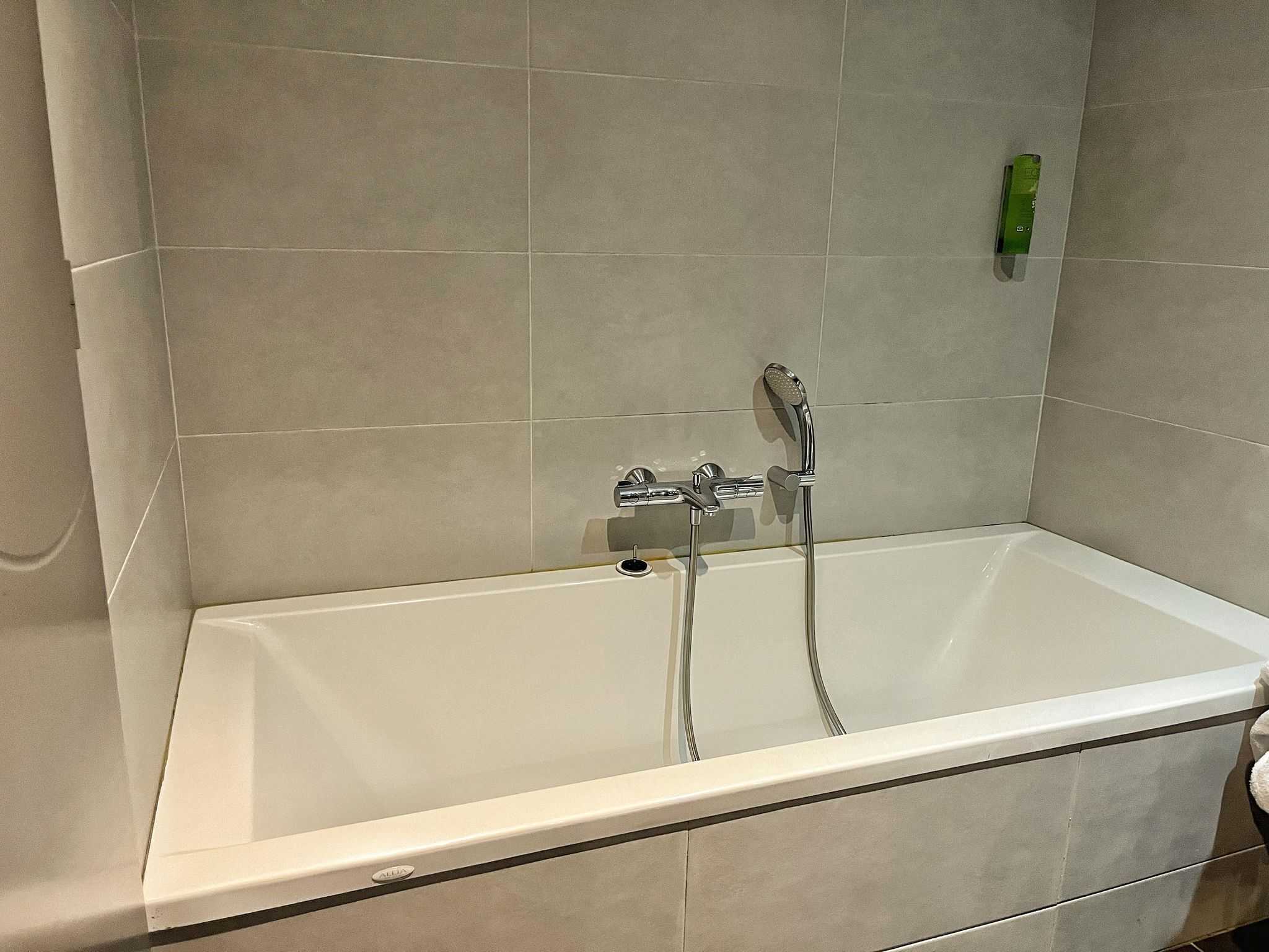 A bathroom with a white bathtub, two showerheads, and a green bottle on the wall.