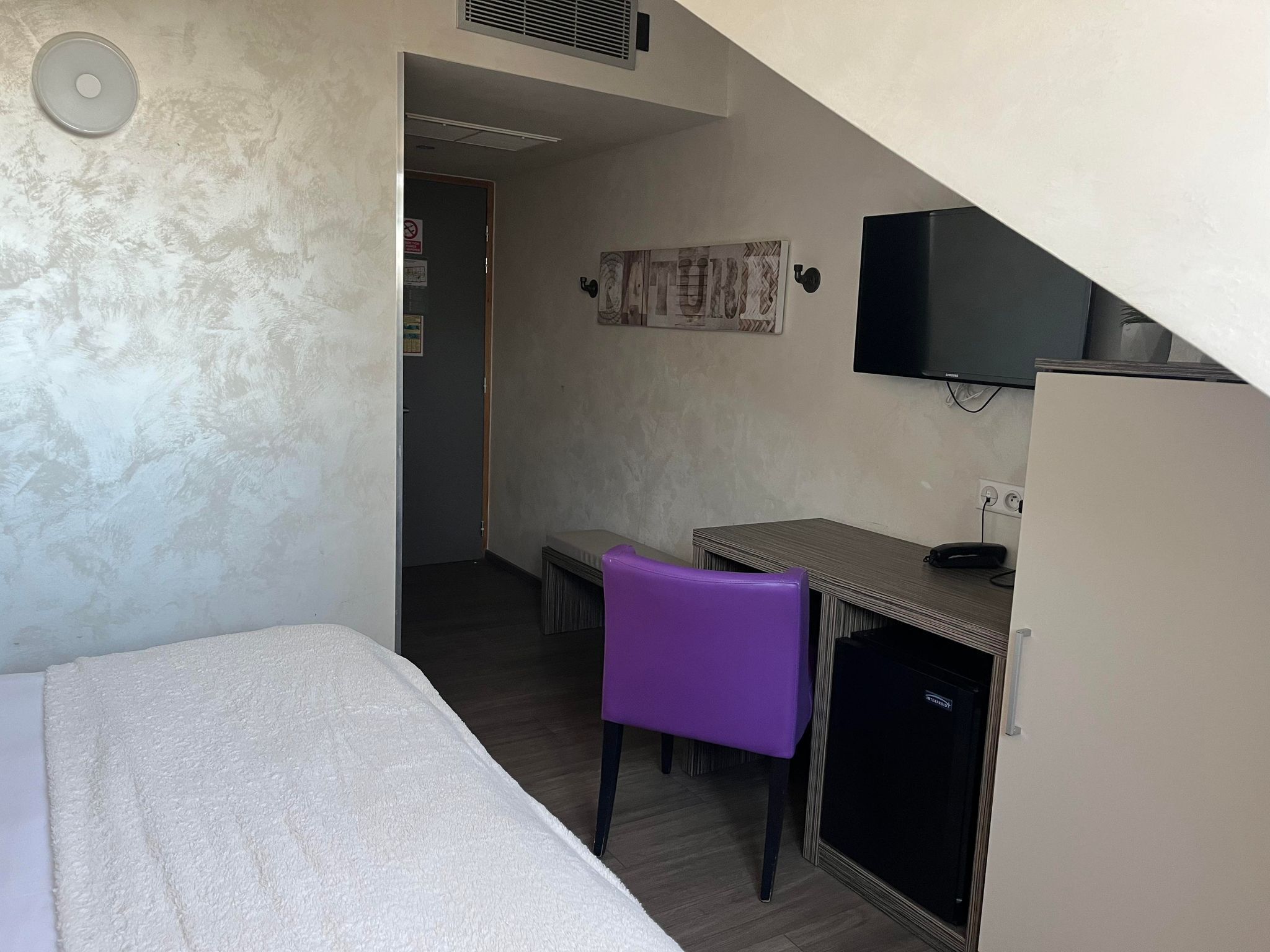 Ein kleiner, gemütlicher Raum mit einem Bett, einem Schreibtisch, einem Stuhl und einem Fernseher.