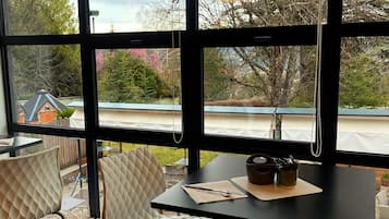 Comedor moderno con una mesa y sillas negras, ventanas amplias con vistas a un jardín y una casa.