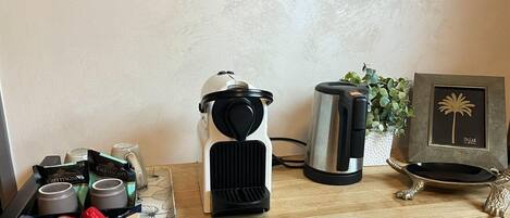 A kitchen counter with a coffee maker, a kettle, a tray with coffee cups, and a decorative item.