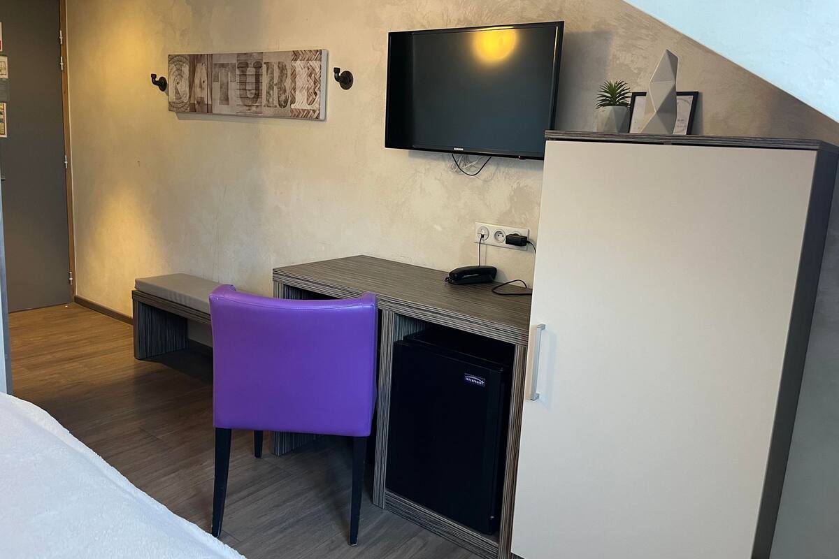 Een kleine hotelkamer met een bed, een bureau met stoel, een televisie en een koelkast.