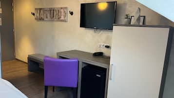 A compact hotel room with a bed, a desk with a chair, a television, and a refrigerator.