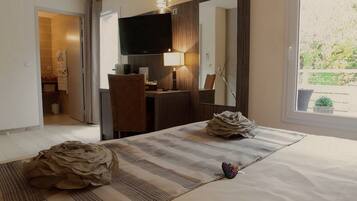 Een hotelkamer met een bed, een bureau, een televisie en een raam met uitzicht op groen.