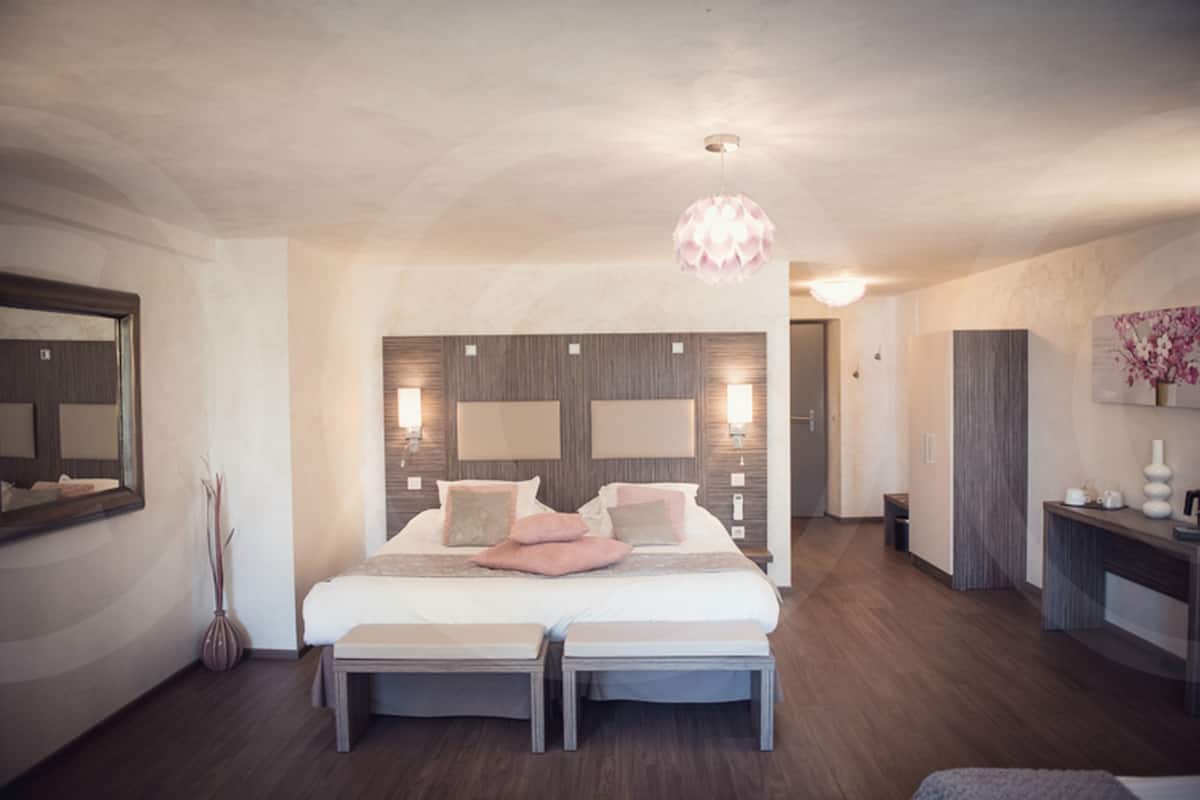 Een moderne slaapkamer met een groot bed, nachtkastjes, een spiegel en een hanglamp.