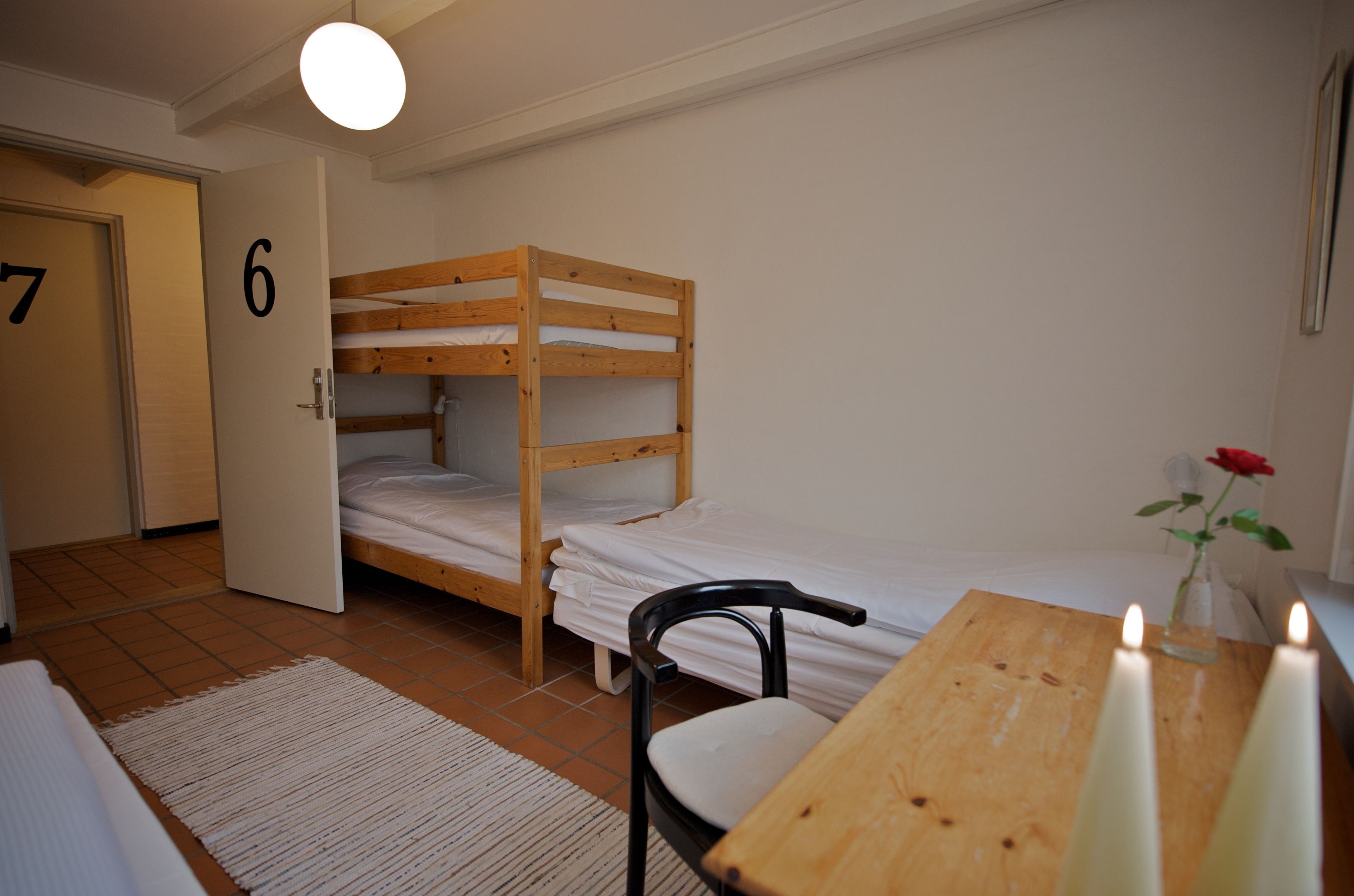 A room with a bunk bed, a wooden table with candles, a chair, and a door marked with the number 6.