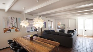 A dining area with a wooden table and chairs, a gray sofa, and a large decorative light fixture. - Benniksgaard Bed & Breakfast (Grasten)