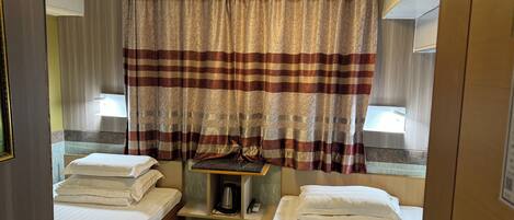 A small, compact hotel room with two single beds, a small table with a kettle, and a ceiling light fixture.