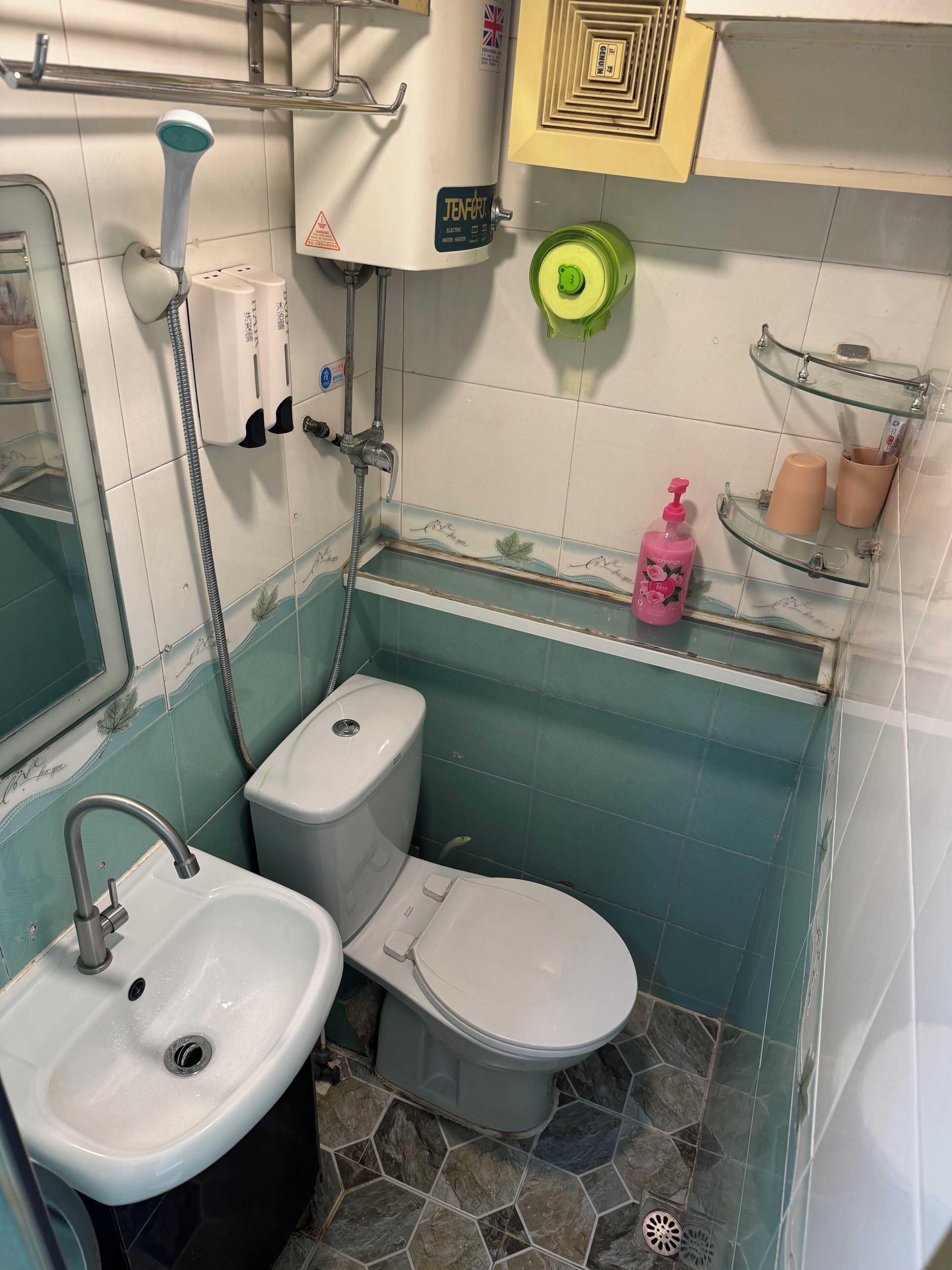 Une salle de bain avec des toilettes, un lavabo et une douche. On y trouve des articles de toilette sur une étagère et un porte-serviettes.