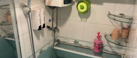 A bathroom with a toilet, sink, and shower. There is a water heater, a soap dispenser, and a glass shelf with toiletries.