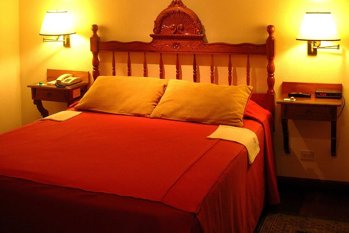 A hotel room with a wooden bed, two bedside tables with lamps, a painting on the wall, and a telephone on one of the tables.