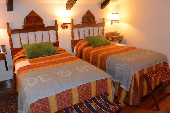 Two double beds with wooden headboards, a nightstand with a lamp, and a bench with hanging clothes.