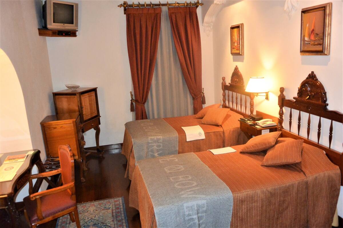 A hotel room with two beds, a desk, a chair, a television, and a lamp.