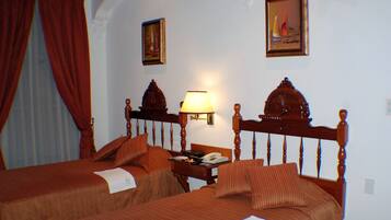 Habitación de hotel con dos camas, una mesita de noche, una lámpara y dos cuadros en la pared.