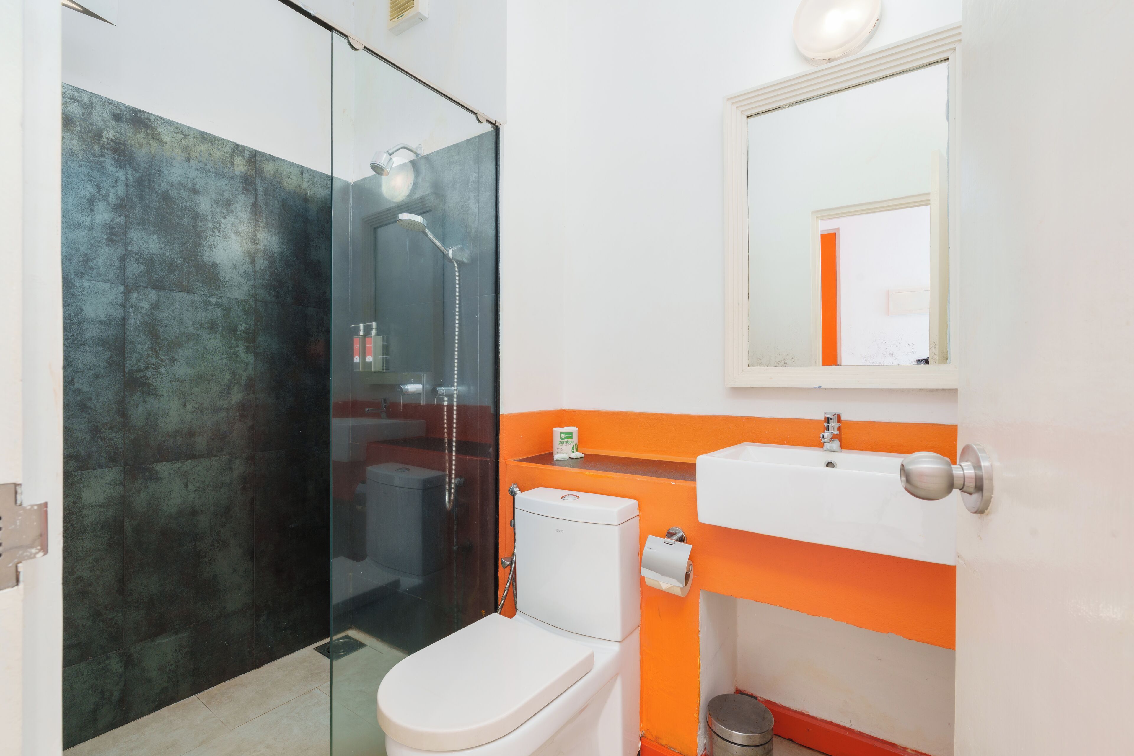 A modern bathroom with a glass shower enclosure, a white toilet, and an orange accent wall.