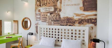 A bedroom with a bed, a desk, and a chair. There is a wall with graffiti and a sign that says "STICK NO BILLS".