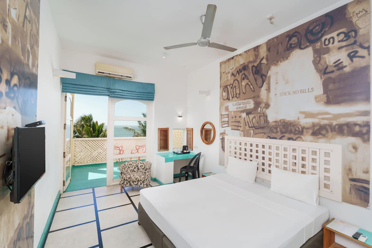 A hotel room with a bed, desk, chair, and a balcony with a view.
