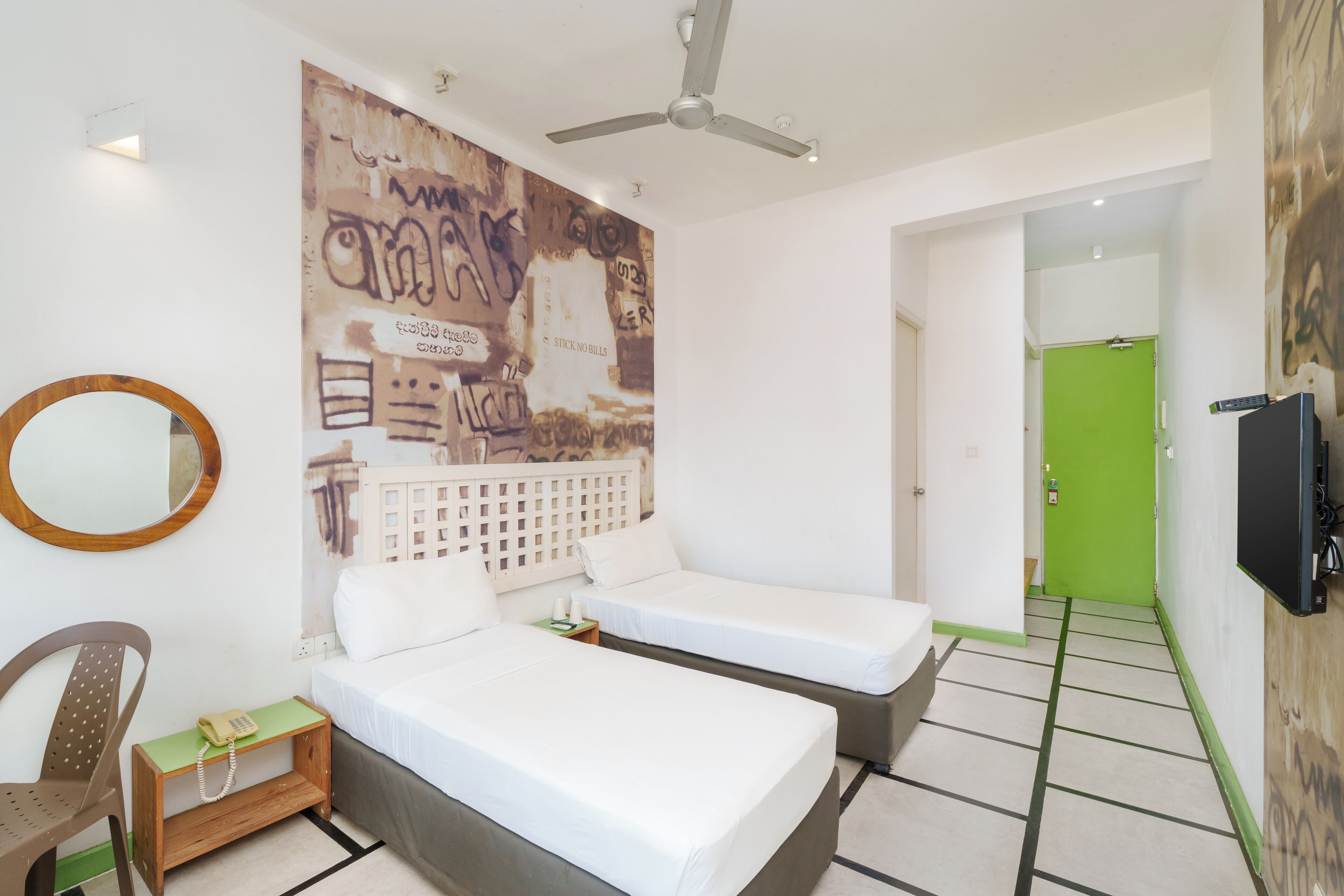 Una habitación con dos camas individuales, una silla de madera, una mesita con teléfono y un amplio mural abstracto en la pared.