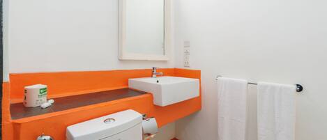 Um banheiro com vaso sanitário branco, pia laranja e espelho sobre ela. Há duas toalhas brancas penduradas em um porta-toalhas.