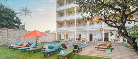 A hotel with a pool area, outdoor lounge chairs, and a multi-story building.