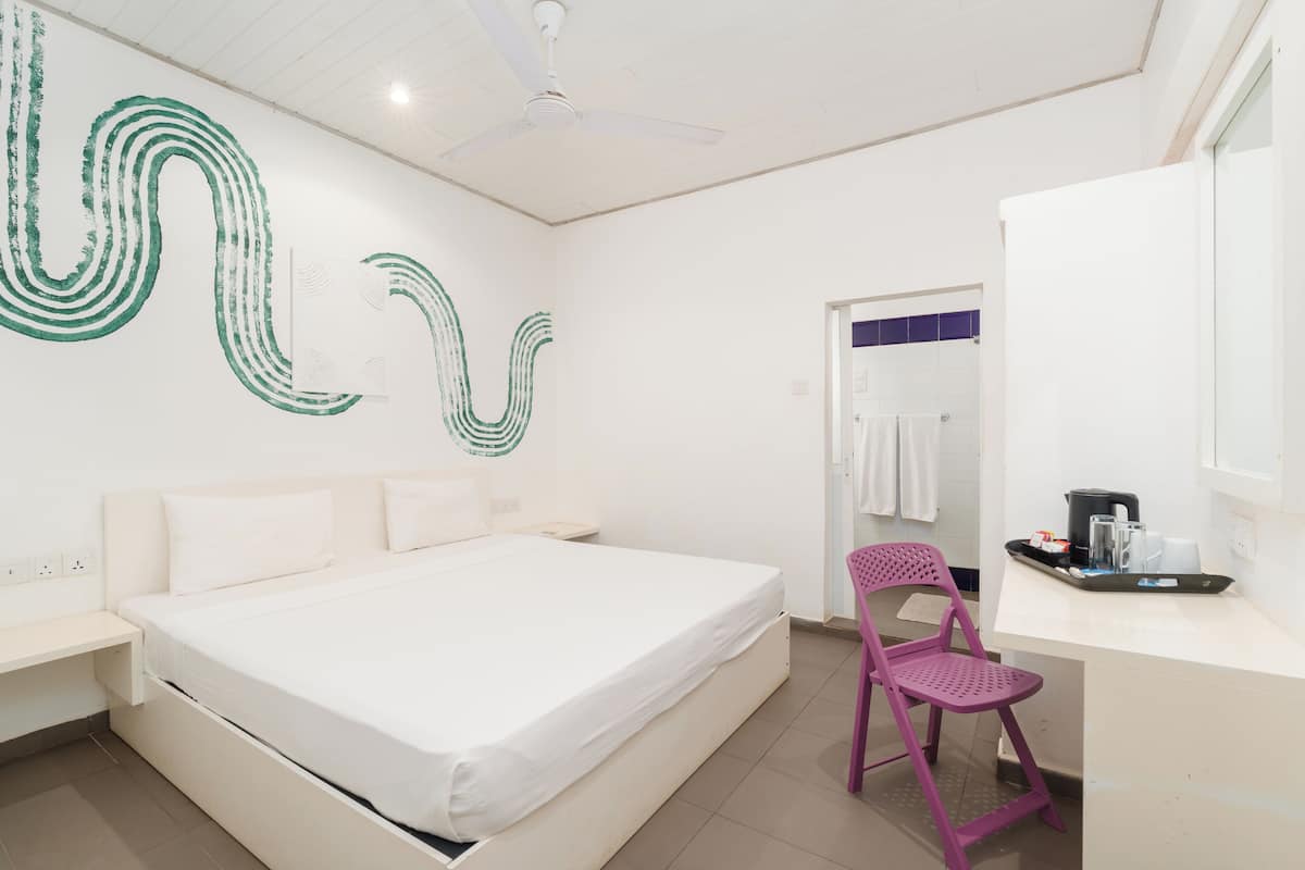 A modern hotel room with a bed, a desk, a chair, and a bathroom visible through an open door.