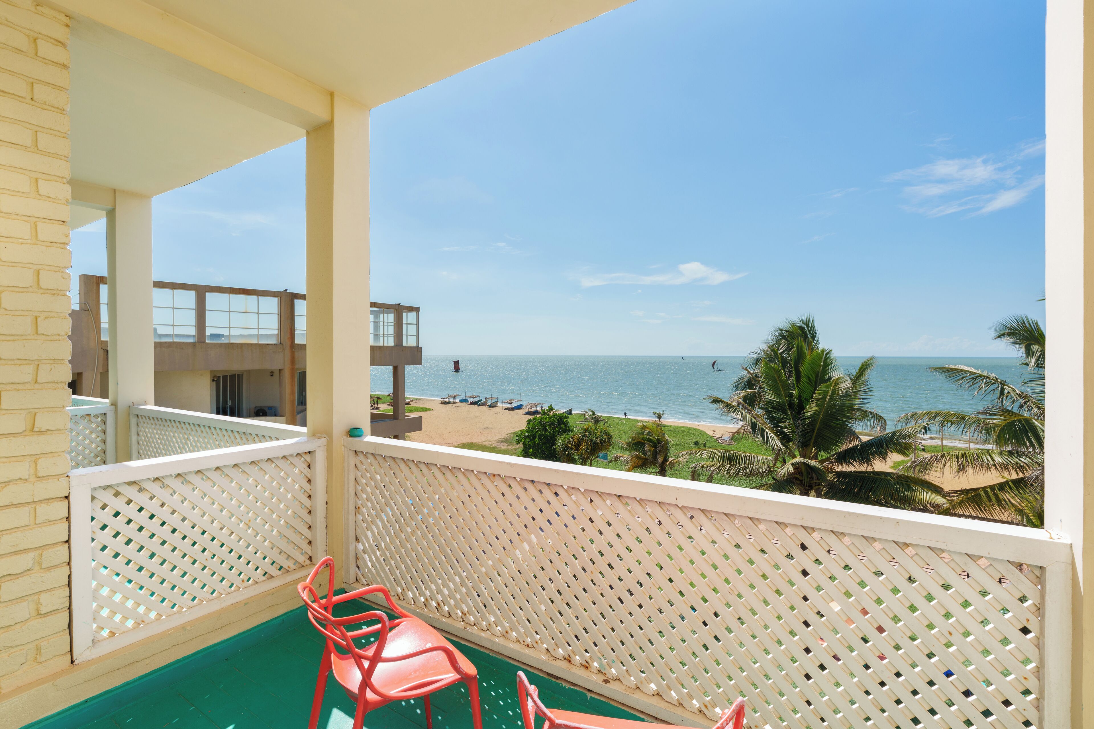 A balcony with a view of the beach, a pool, and a building in the background.