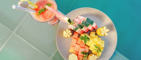 Un plato de frutas cortadas y un vaso de bebida rosa con pajita.