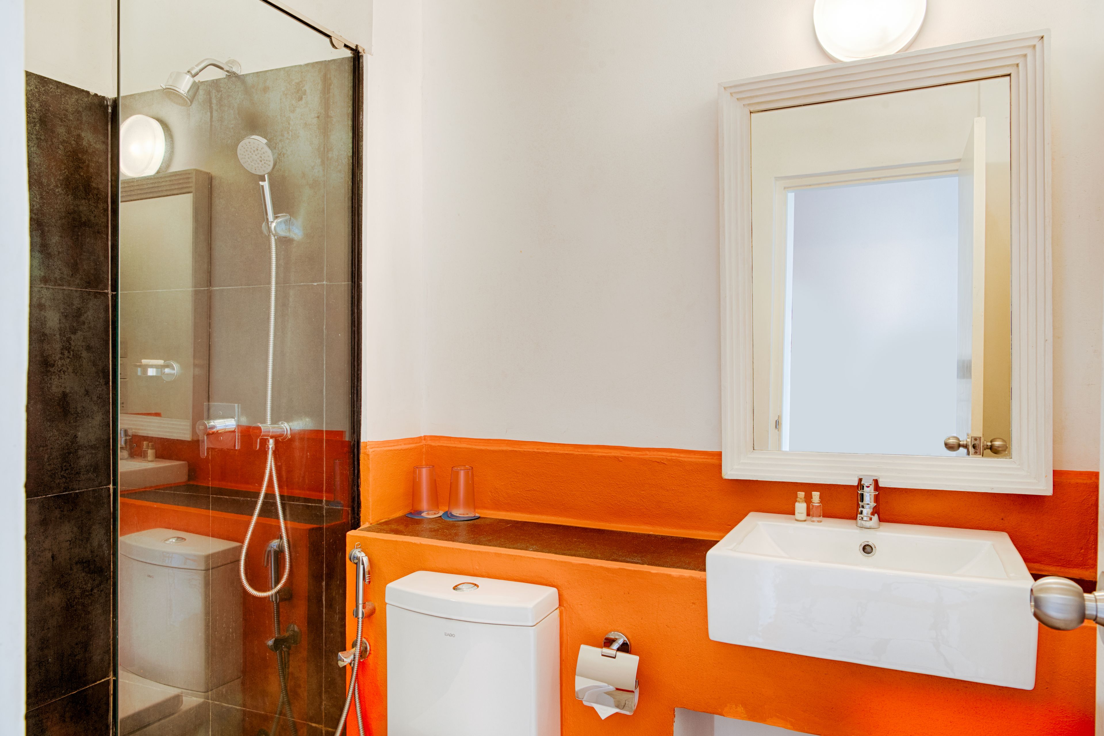 A bathroom with a glass-enclosed shower, a white sink, and an orange accent wall.