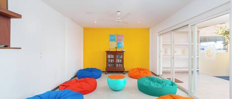 Une pièce avec des fauteuils en forme de sac de haricots aux couleurs vives, disposés en cercle, un petit meuble en bois contenant des livres et une porte en verre donnant sur l’extérieur.