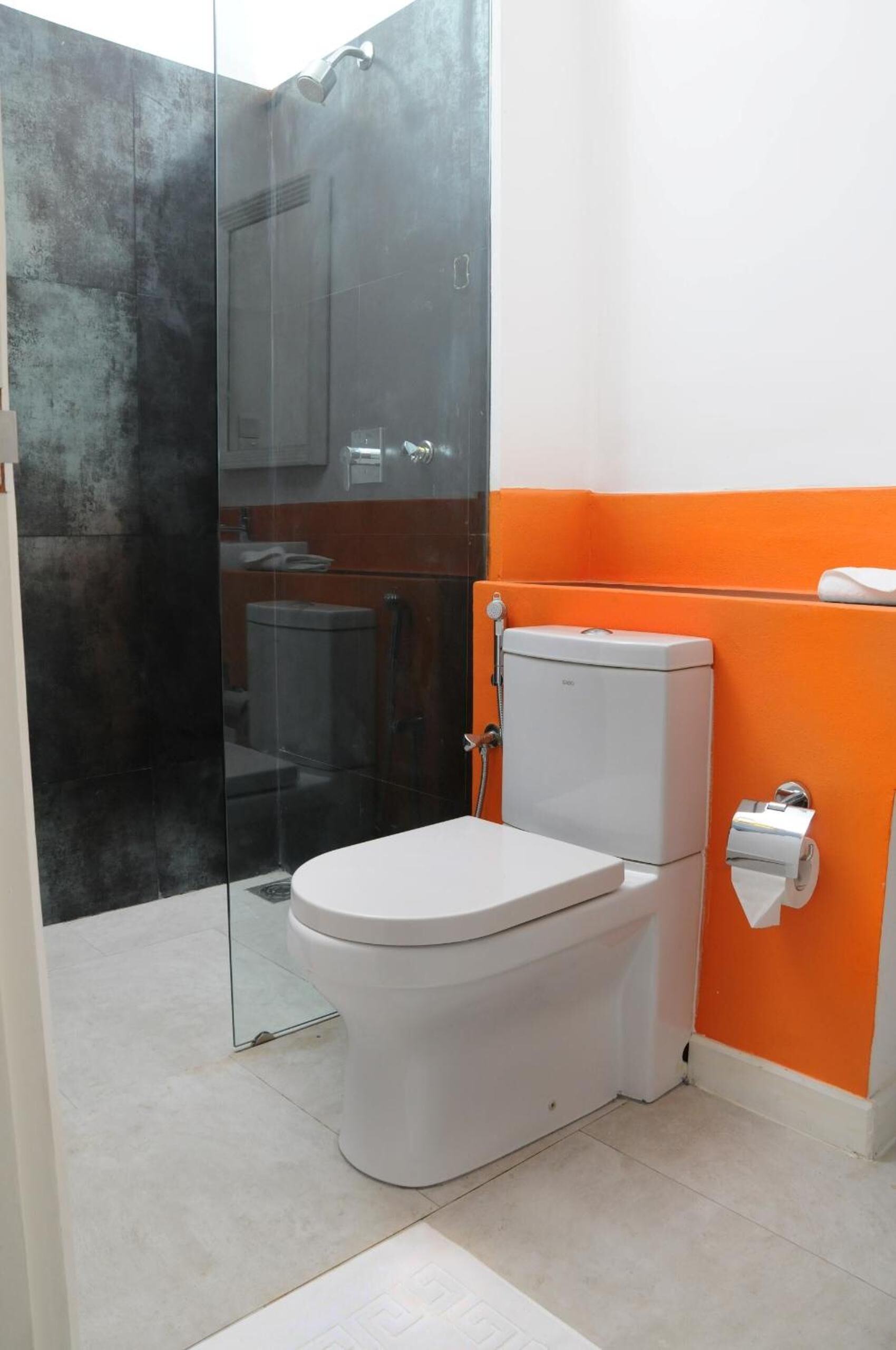 A bathroom with a toilet, a glass shower enclosure, and an orange accent wall.