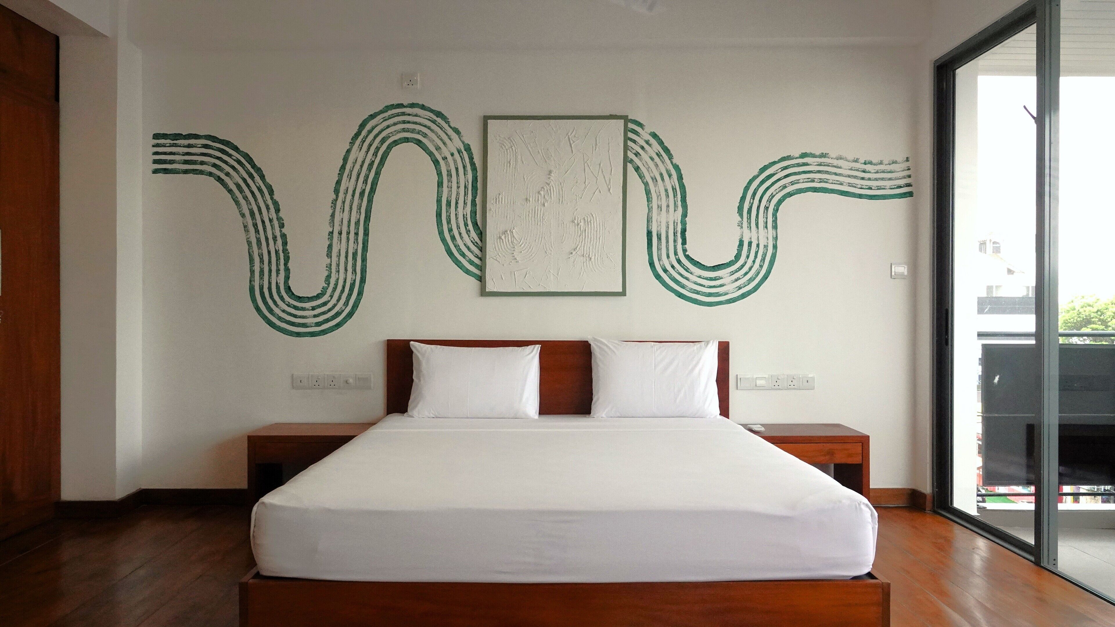 A modern hotel room with a large bed, wooden headboard, and a view through a large window.