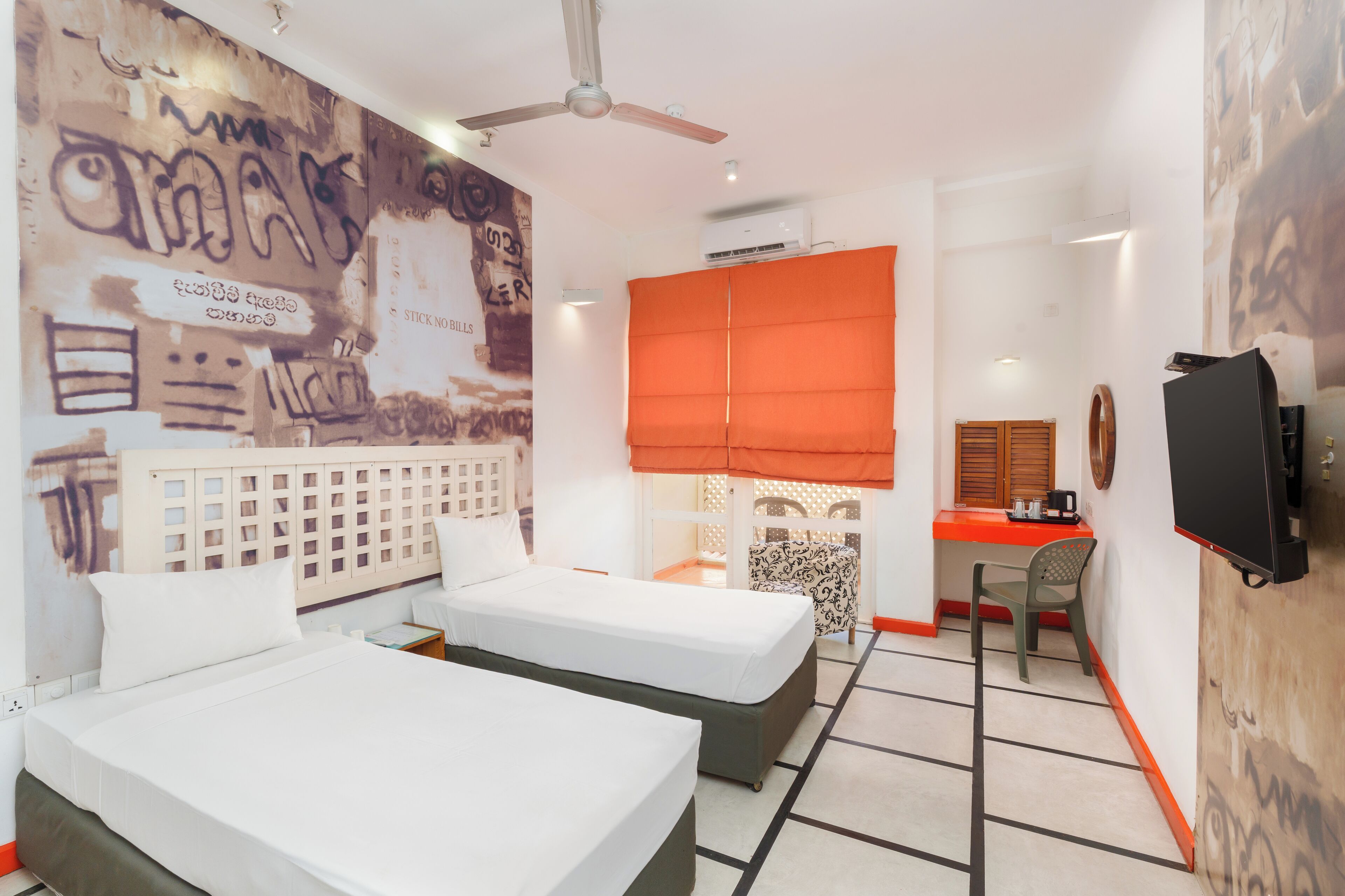 A hotel room with two beds, a desk, a chair, a television, and a ceiling fan.