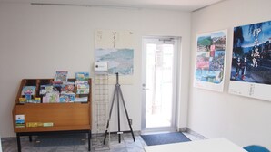 A room with a wooden cabinet filled with brochures, a tripod, and a white table. - Hotel Redent Ito (Ito)
