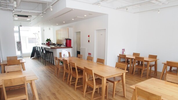 A spacious room with wooden tables and chairs, a kitchen area with a refrigerator and coffee machine, and a visible toilet sign. - Hotel Redent Ito (Ito)