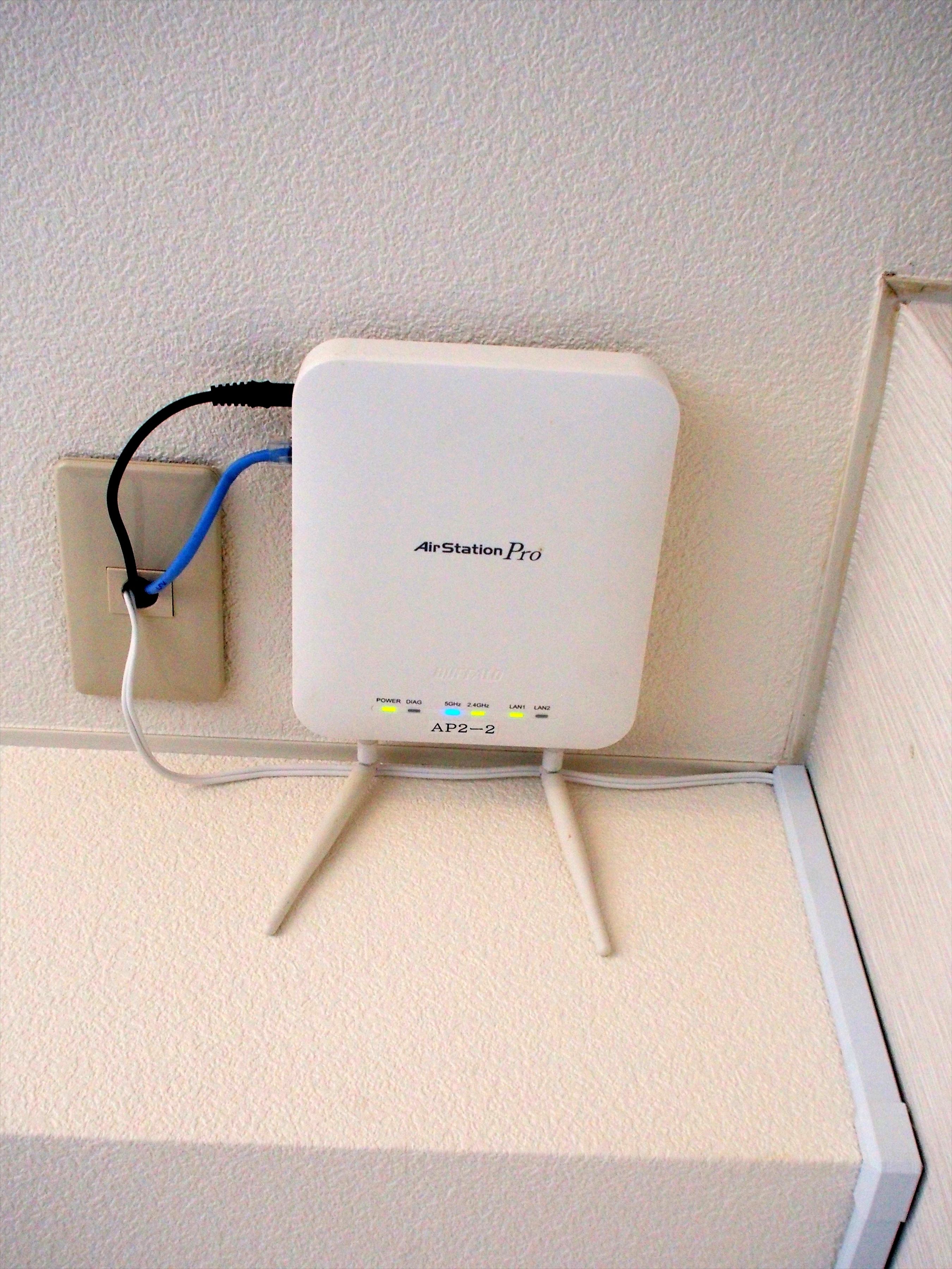 An AirStation Pro device mounted on a wall with a power cord plugged into a nearby electrical outlet.