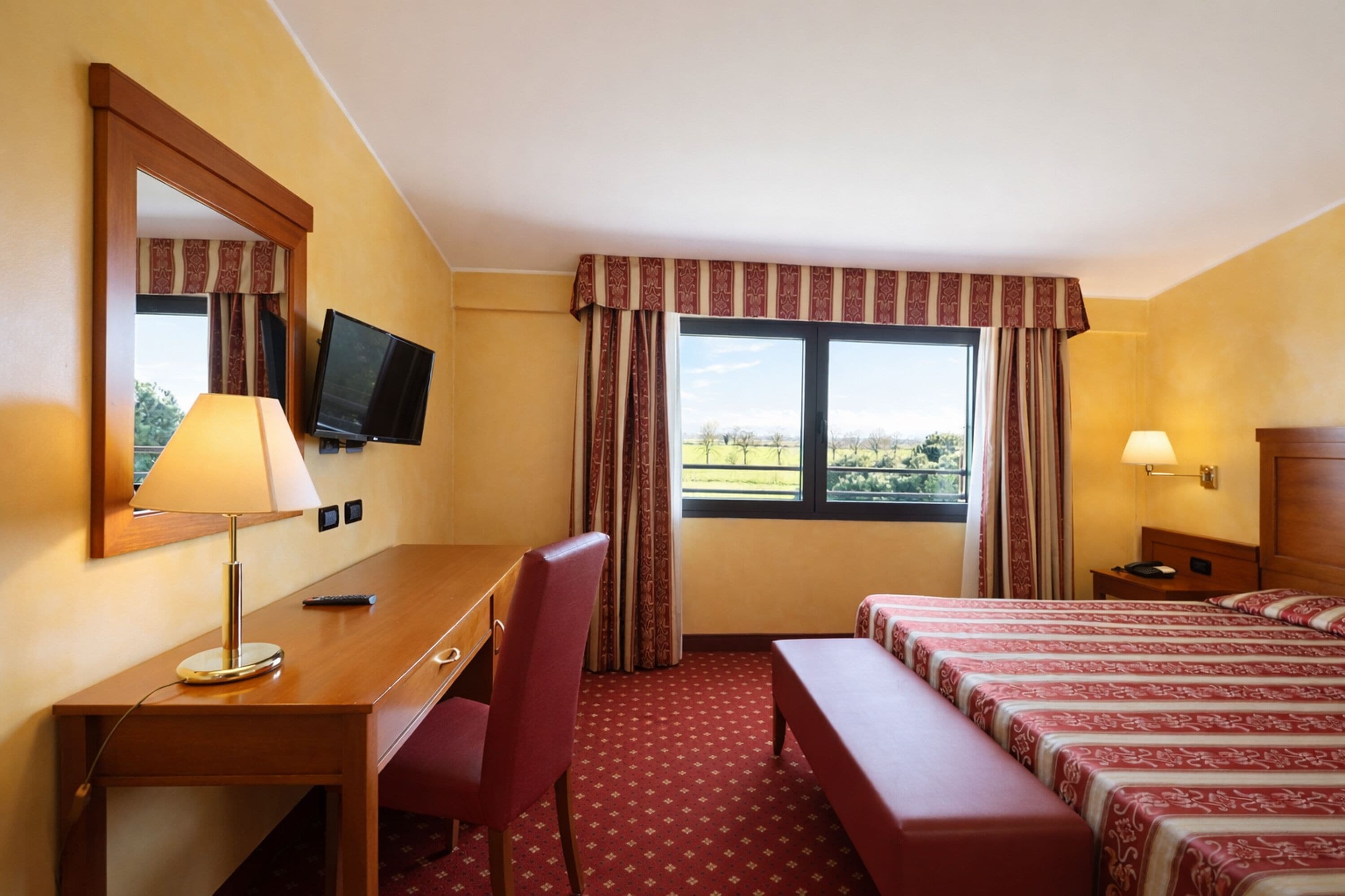 Habitación de hotel con escritorio, silla, dos camas, televisión y ventana con cortinas.