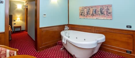 Un baño con bañera, paneles de madera, piso estampado rojo, un cuadro en la pared y una puerta que da a otra habitación.