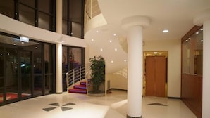 A spacious lobby with a modern design, featuring a central staircase, a large potted plant, and a glass entrance. - LVG Hotel Collection – Riz (San Genesio ed Uniti)